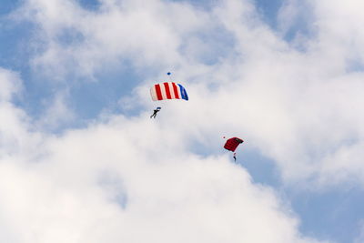 Low angle view of people paragliding against sky