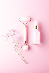 Composition of mockup serum bottle, pink quartz stone face roller with gipsophyla flowers on pink 