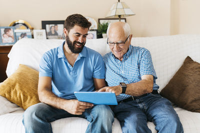 Adult grandson teaching his grandfather to use tablet