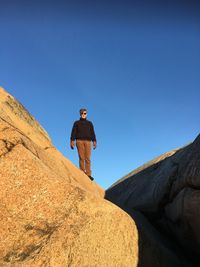 Low angle view of man standing on rock against clear blue sky