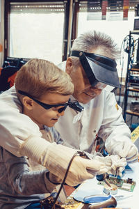 Engineering teacher and kid soldering mother board in tech workshop.