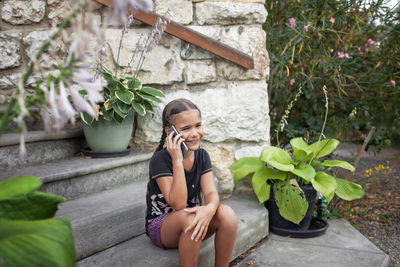 Young woman using mobile phone while sitting against plants