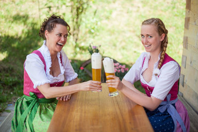 Portrait of smiling young woman with friend toasting beer at table