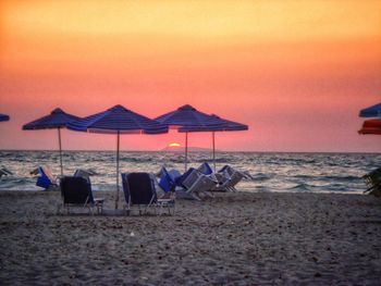 Chairs on beach against sky during sunset