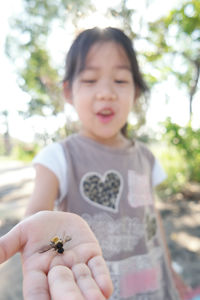 Girl showing bee on palm while standing against trees