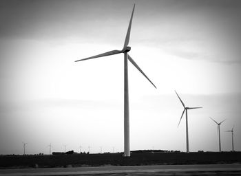 Low angle view of wind turbines on field against sky
