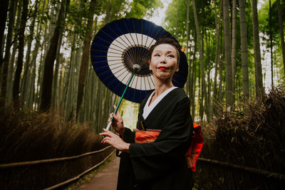 Mature woman with umbrella standing amidst trees