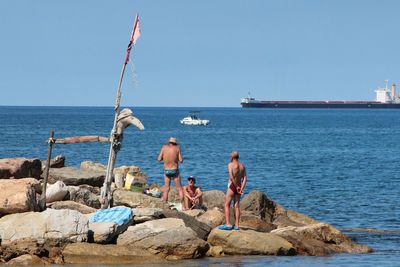 Rear view of men on rocks by sea against clear sky