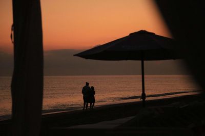 Silhouette people on beach against sky during sunset