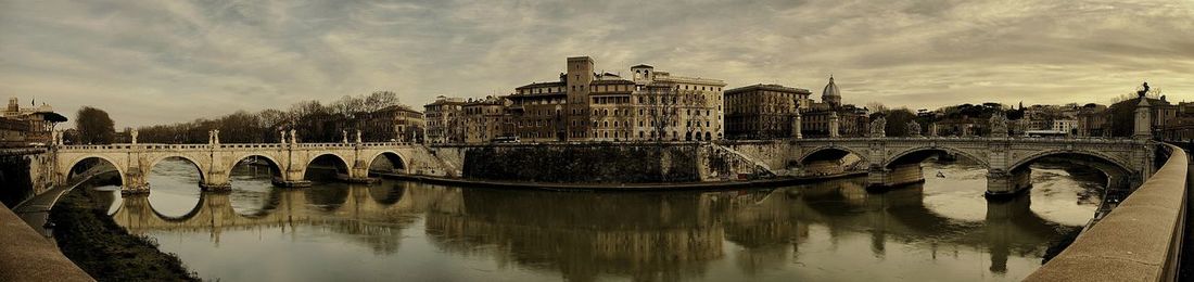 Arch bridge over river by buildings against sky