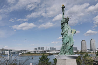 Statue of liberty in city against cloudy sky