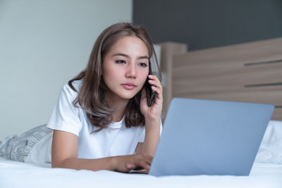Portrait of young woman using mobile phone while sitting on bed
