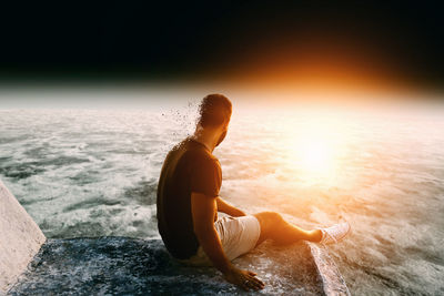 Man relaxing on beach against sky during sunset