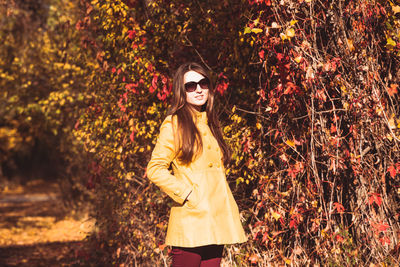 Portrait of young woman wearing sunglasses standing by plants during autumn