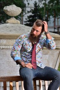 Hipster looking away while sitting on bench at park
