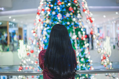 Rear view of woman looking at illuminated christmas tree in shopping mall
