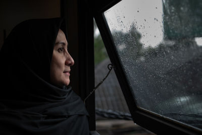 Close-up of woman looking away while standing by window during rain