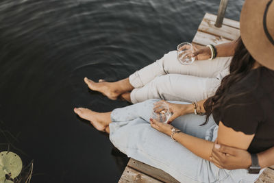 Boyfriend and girlfriend drinking wine while sitting on pier