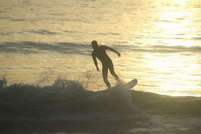 Silhouette man surfing in sea against sky during sunset