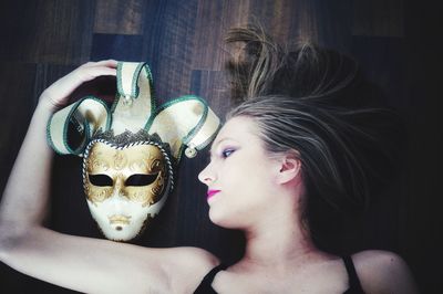 Directly above shot of beautiful woman lying down by mask on hardwood floor