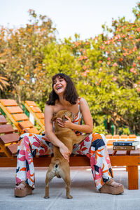 Young woman with dog sitting outdoors next to a pool, in summertime.