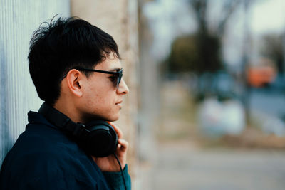Side portrait of good looking man wearing sunglasses and headphones standing against a wall