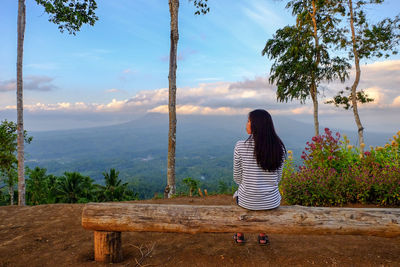 Rear view of woman sitting by plants against sky