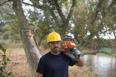 Man wearing hardhat carrying chainsaw in forest