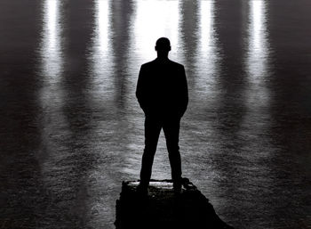 Rear view of silhouette man standing by lake at night