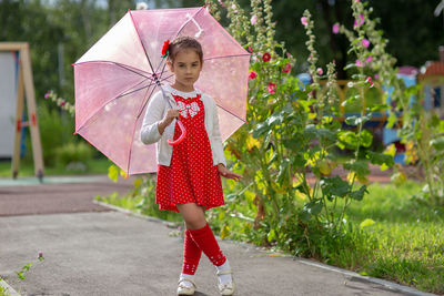 A beautiful little girl in a red dress and a pink umbrella