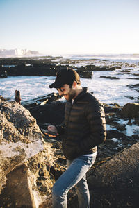 Man standing on rock at shore against clear sky