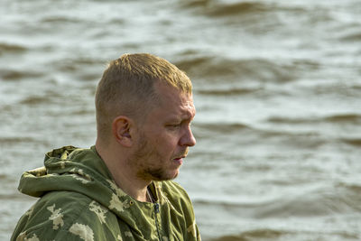 Unshaven fisherman against background of waves on river looks forward. side view.