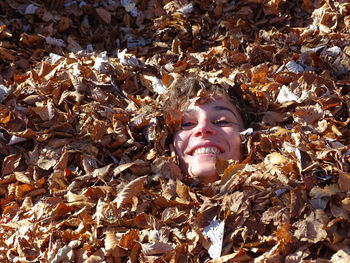 Close-up of young woman covered with dry leaves