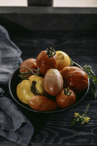 Multicolored tomatoes of different sizes and types in a dark dish and rustic background