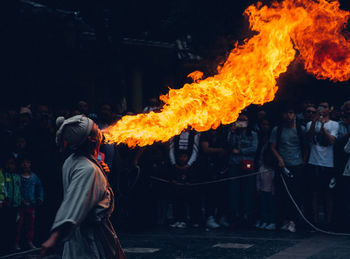 Fire breather blowing fire while standing outdoors at night