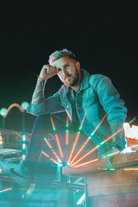 Portrait of man sitting by illuminated light at night