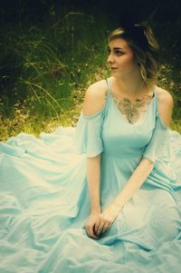 Young beautiful woman wearing blue evening gown while sitting on field