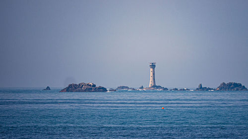 Lighthouse by sea against clear sky