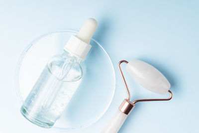 Face massage roller with serum or essential oil bottle on blue background. flat lay, top view