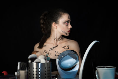 Woman with text on body sitting against black background