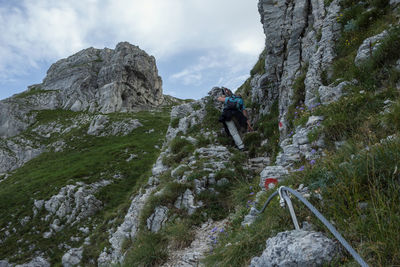 Woman walking on rocks by mountains against sky