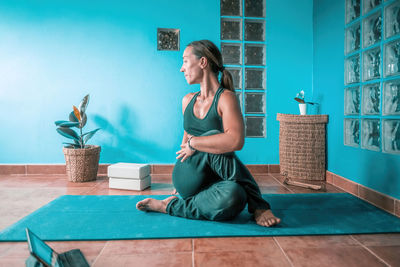 Full length of woman sitting on floor against wall
