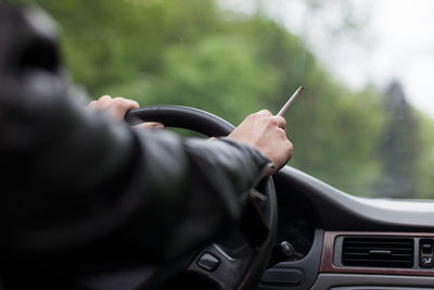 Close-up of woman smoking cigarette while driving car against tree