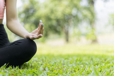 Midsection of woman meditating while sitting on grassy field at park