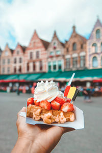 Cropped image of hand holding dessert against buildings