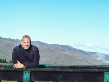 Portrait of smiling man standing on mountain against clear sky