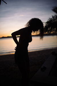 Silhouette woman standing at beach against sky during sunset