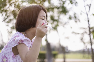 Side view of girl blowing bubbles in park