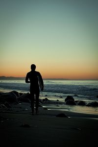 Silhouette man with surfboard at beach against sky during sunset