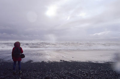 Rear view of woman standing on beach against sky